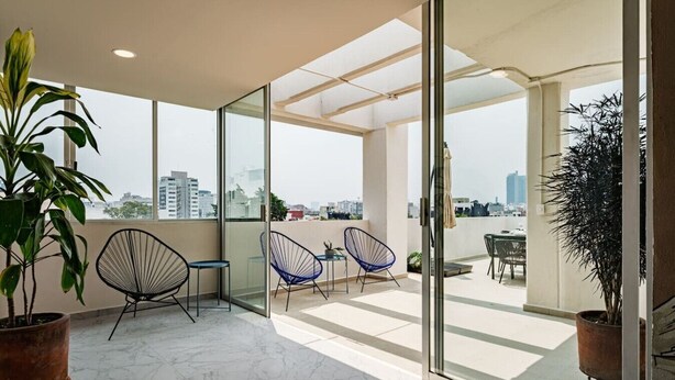 A modern balcony with glass doors, potted plants, and seating. - Roma Sur Stay: Private Elevator, BBQ & Rooftop (Mexico City)