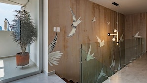A modern interior with a large potted plant, a wall with bird mural, and a glass railing with a reflection. - Roma Sur Stay: Private Elevator, BBQ & Rooftop (Mexico City)
