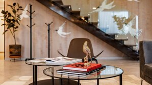 A modern interior with a glass table displaying books and a decorative bird sculpture, a staircase with white bird wall art, and a potted plant. - Roma Sur Stay: Private Elevator, BBQ & Rooftop (Mexico City)