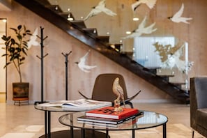 Ein modernes Interieur mit einem Glastisch, der Bücher und eine dekorative Vogel-Skulptur zeigt, einer Treppe mit Vogel-Wandbildern und einem Blumentopf.
