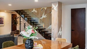 A modern interior with a wooden dining table, a vase with flowers, a staircase with a wooden railing, and a dark wooden door. - Roma Sur Stay: Private Elevator, BBQ & Rooftop (Mexico City)
