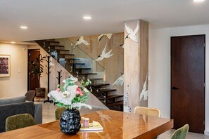 Ein modernes Interieur mit einem Holzespeisetisch, einer Blumenvase, einer Treppe mit Holzwandlaufgeländer und einer dunklen Holztür.