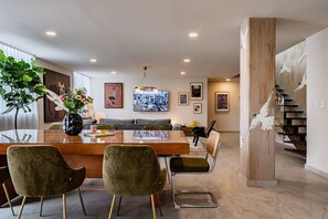 Ein modernes Wohnzimmer mit Essbereich, ausgestattet mit einer Couch, einem Glastisch und einer Treppe mit Dekorationselementen.
