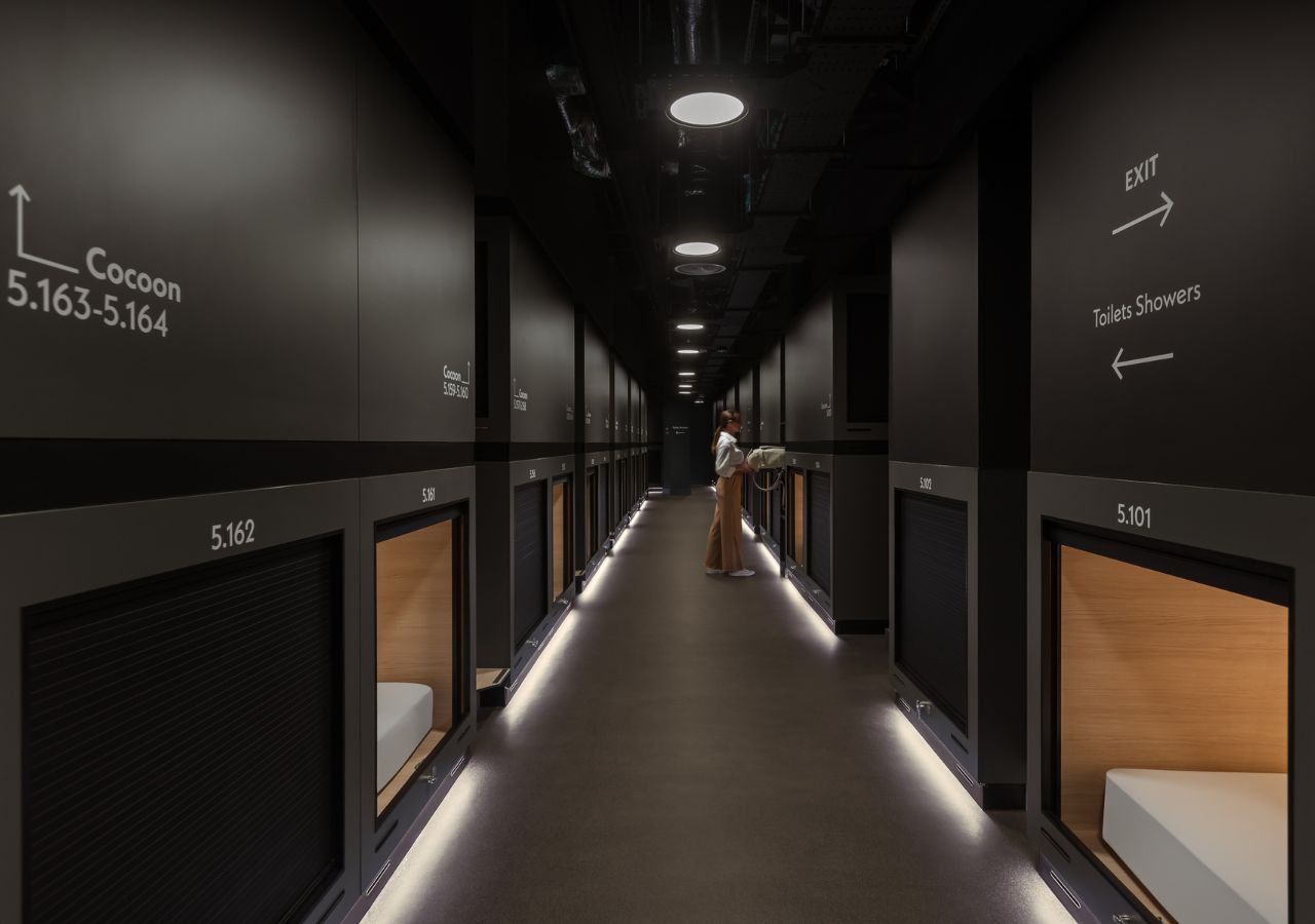 A hotel corridor with numbered rooms, directional signs for toilets and showers, and a person walking.
