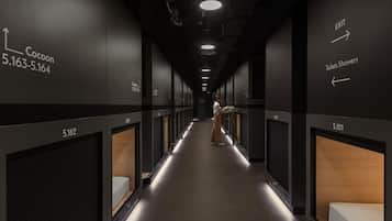 Een hotelgang met genummerde kamers, pijlen naar toiletten en douches, en een persoon die loopt.