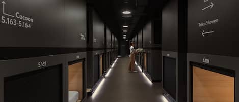A hotel corridor with numbered rooms, directional signs for toilets and showers, and a person walking.