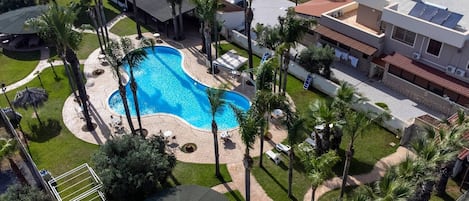 Una piscina rodeada de palmeras y una terraza cubierta.