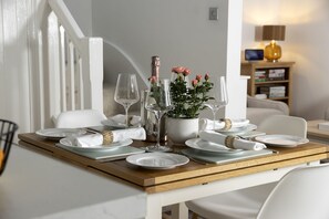 Une table à manger dressée avec des assiettes, des couverts et des verres à vin, et un vase de fleurs placé au centre.