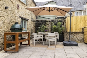 Eine Terrasse mit Tisch, Stühlen, einem Grill und einem großen Sonnenschirm.