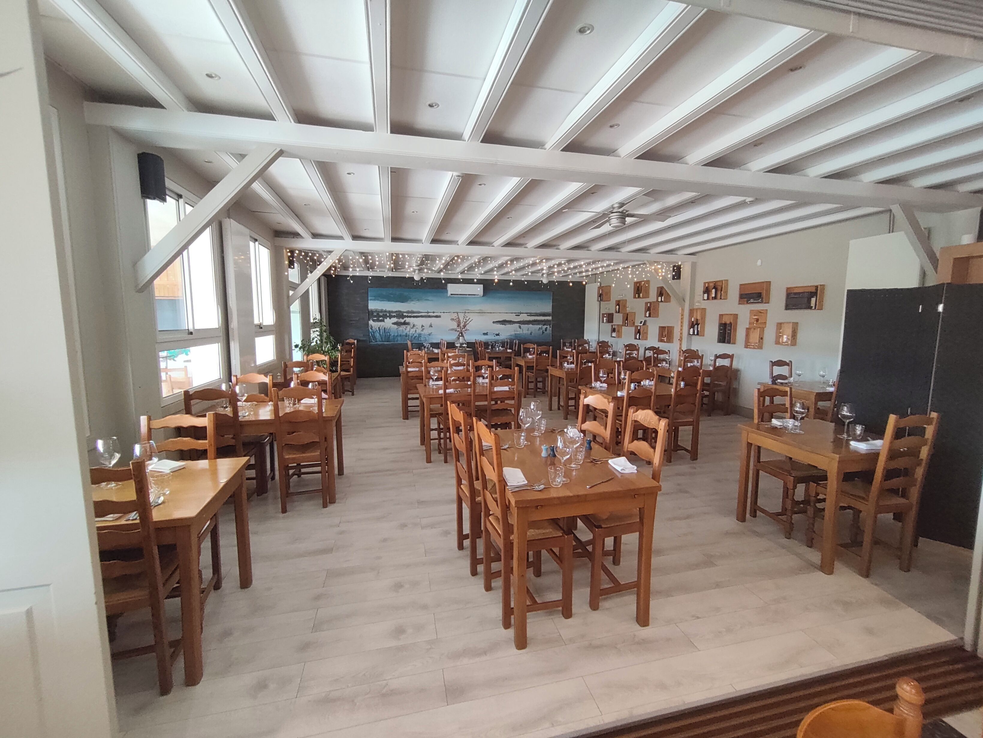 Un vaste espace dédié à la salle à manger, avec de nombreuses tables et chaises en bois, un plafond avec des poutres apparentes et une grande fresque murale sur le mur du fond.