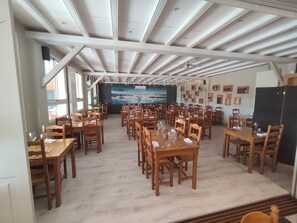 Un comedor amplio con varias mesas y sillas de madera, un techo con vigas a la vista y un mural grande en la pared del fondo.