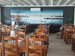 A restaurant with wooden tables and chairs, a large painting of a landscape on the wall, and an air conditioning unit. - Logis Hôtel Auberge de la Gabrière (Lingé)