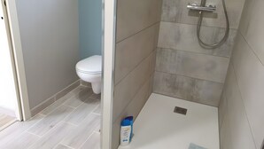 Een badkamer met een wit toilet, een douchegedeelte met een handdouche en een fles douchegel op de vloer.