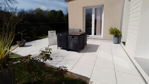 Een terras met een tafel, stoelen, een plant in pot en een schuifdeur.