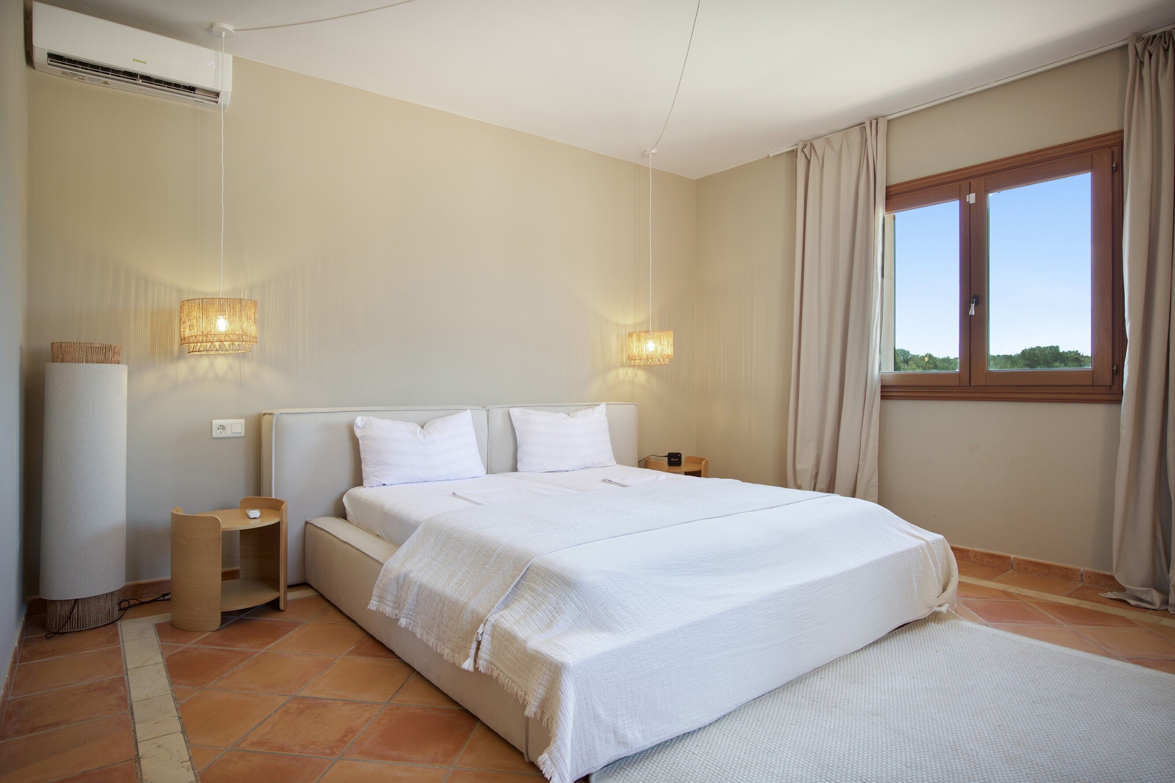 Hotelkamer met een bed, nachtkastjes, een raam met gordijnen en een wandairconditioner.