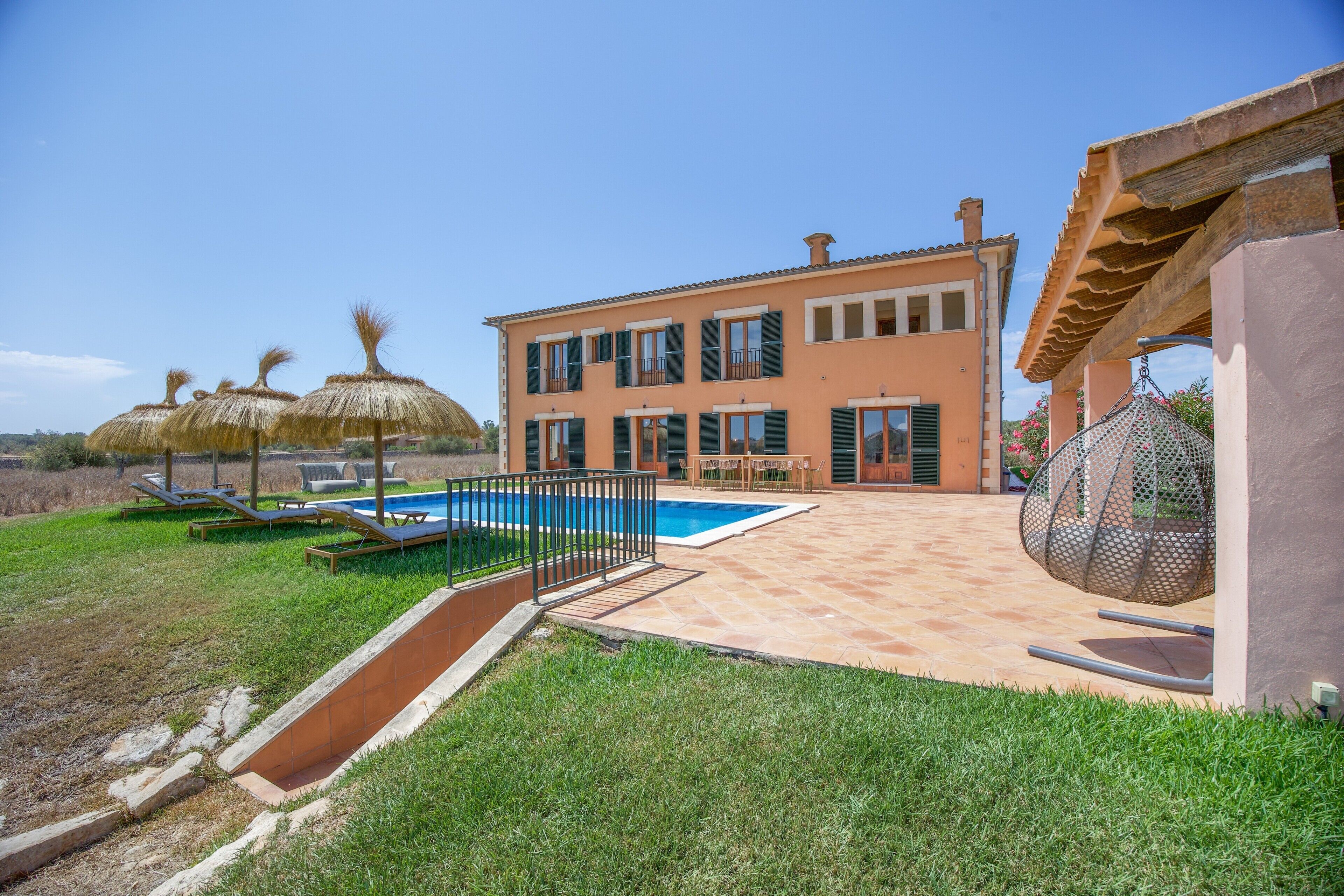 A two-story house with a swimming pool, outdoor seating, and a well-maintained lawn.