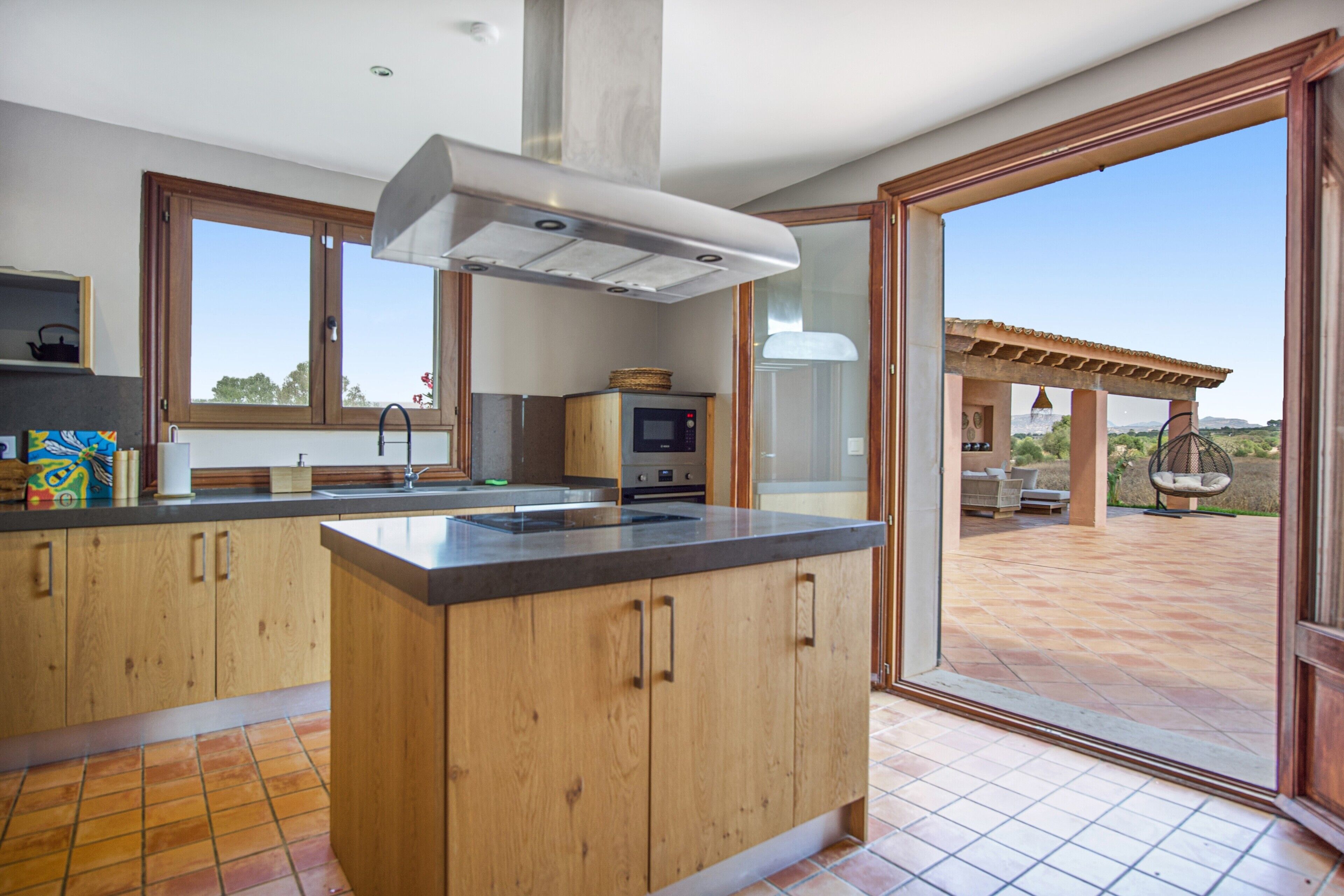 Eine moderne Küche mit Holzschränken, einer großen Kochinsel und Blick auf die Terrasse.