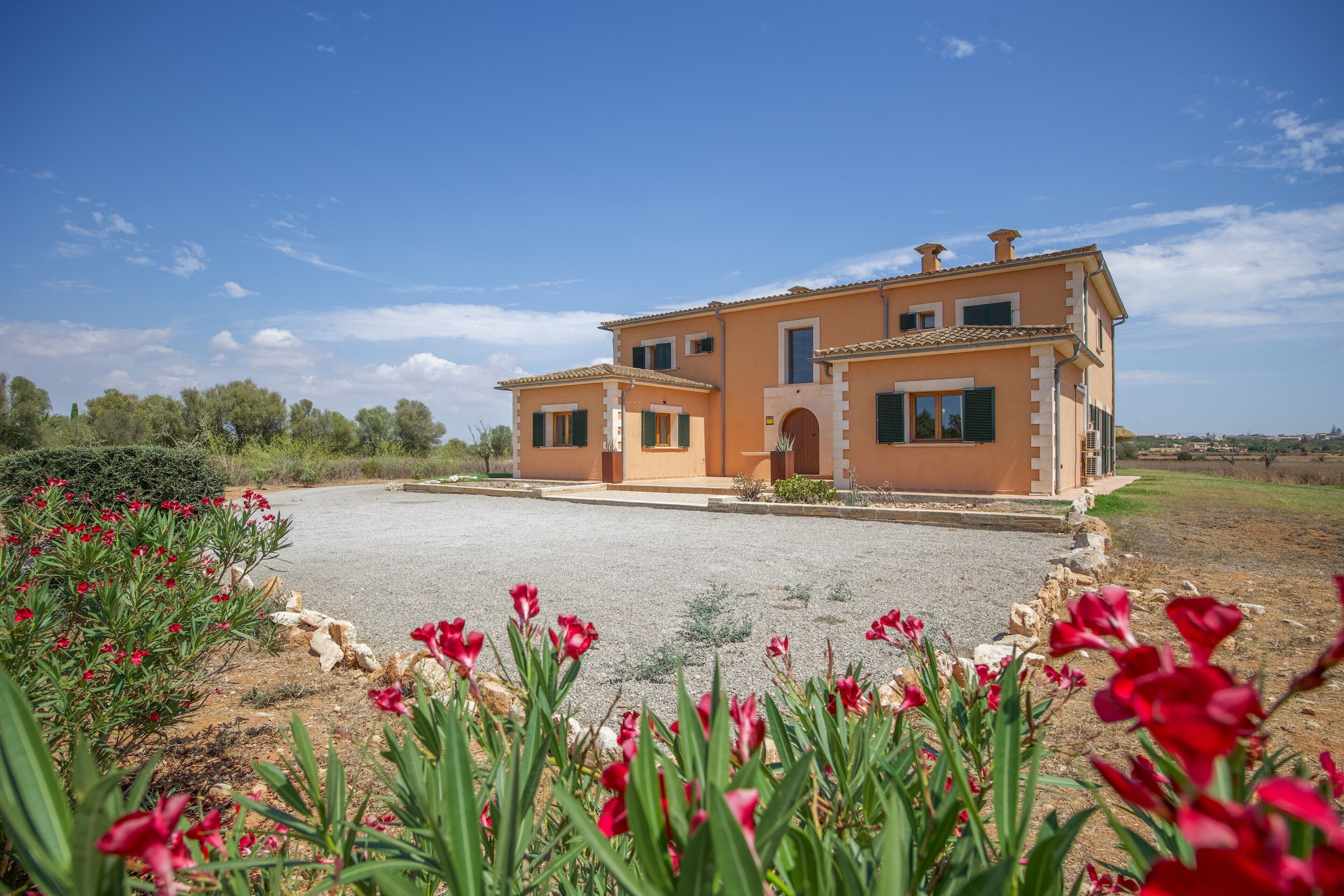 A two-story house with a gravel driveway and a garden with red flowers.
