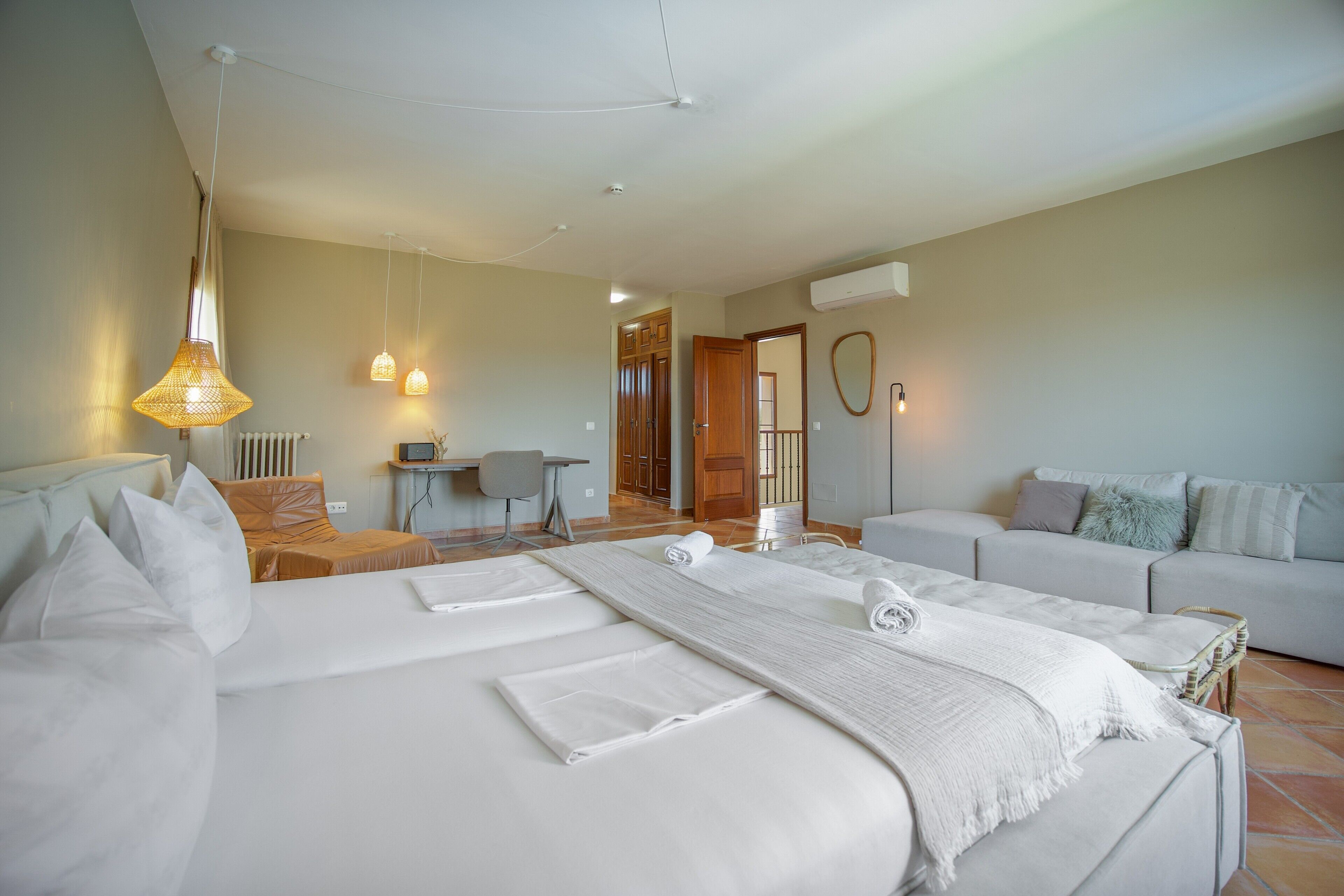 Een hotelkamer met een groot bed, een bank, een bureau en een stoel. Er is een raam, een deur en een airconditioning op de muur.