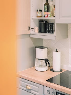 A kitchen with a coffee maker, a roll of paper towels, and various condiments on the shelves.