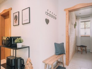 A room with a wooden bench, a small table with a kettle and toaster, a wall-mounted coat rack, and framed pictures.