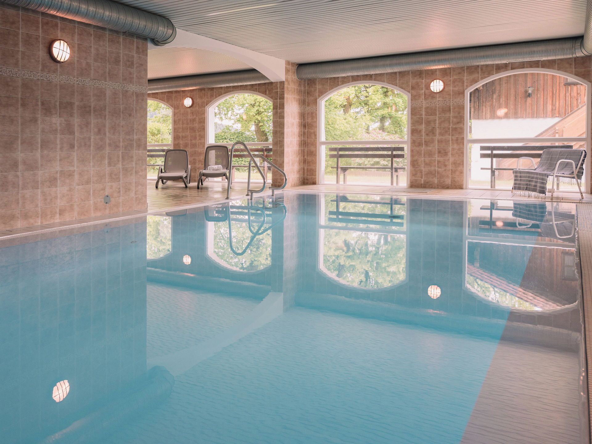 An indoor swimming pool with clear water, surrounded by walls with large windows and doors.