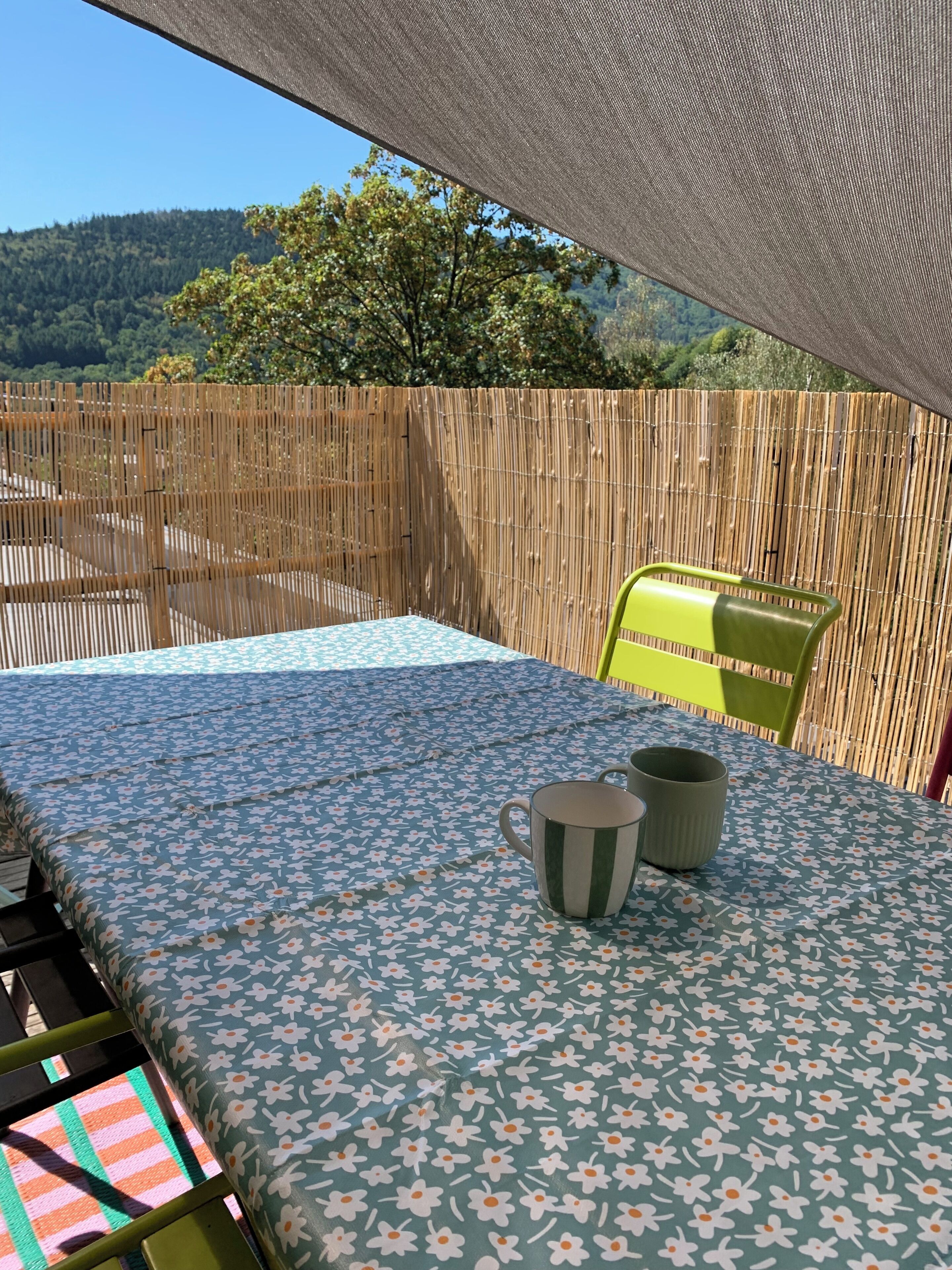 Un espace patio avec une table recouverte d’une nappe à motifs floraux, une chaise et une tasse.