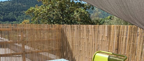 Uma área de pátio com uma mesa coberta por uma toalha de mesa florida, uma cadeira e uma xícara.