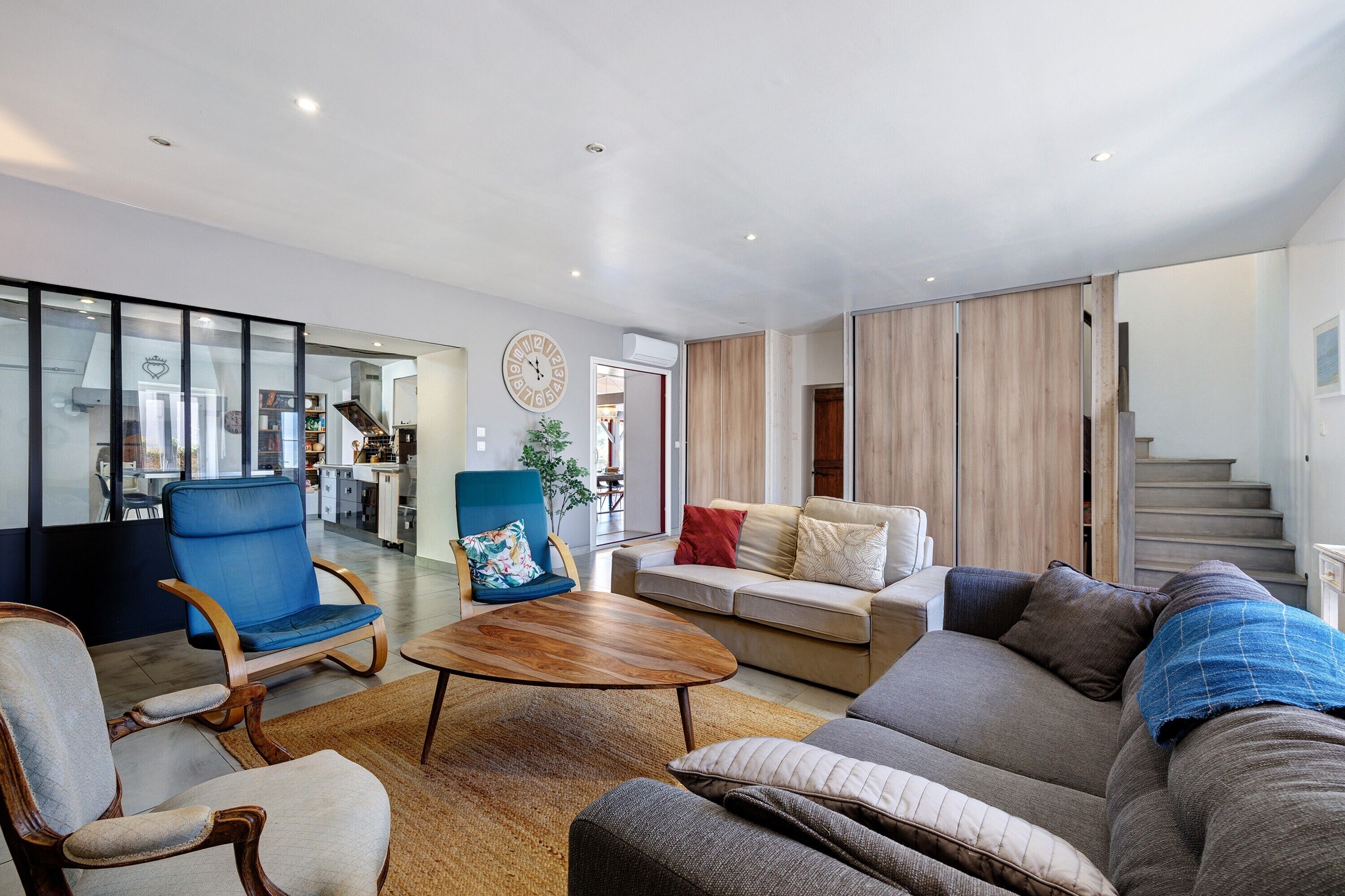 A modern living room with a sofa, armchairs, a coffee table, and a dining area with a kitchen in the background.