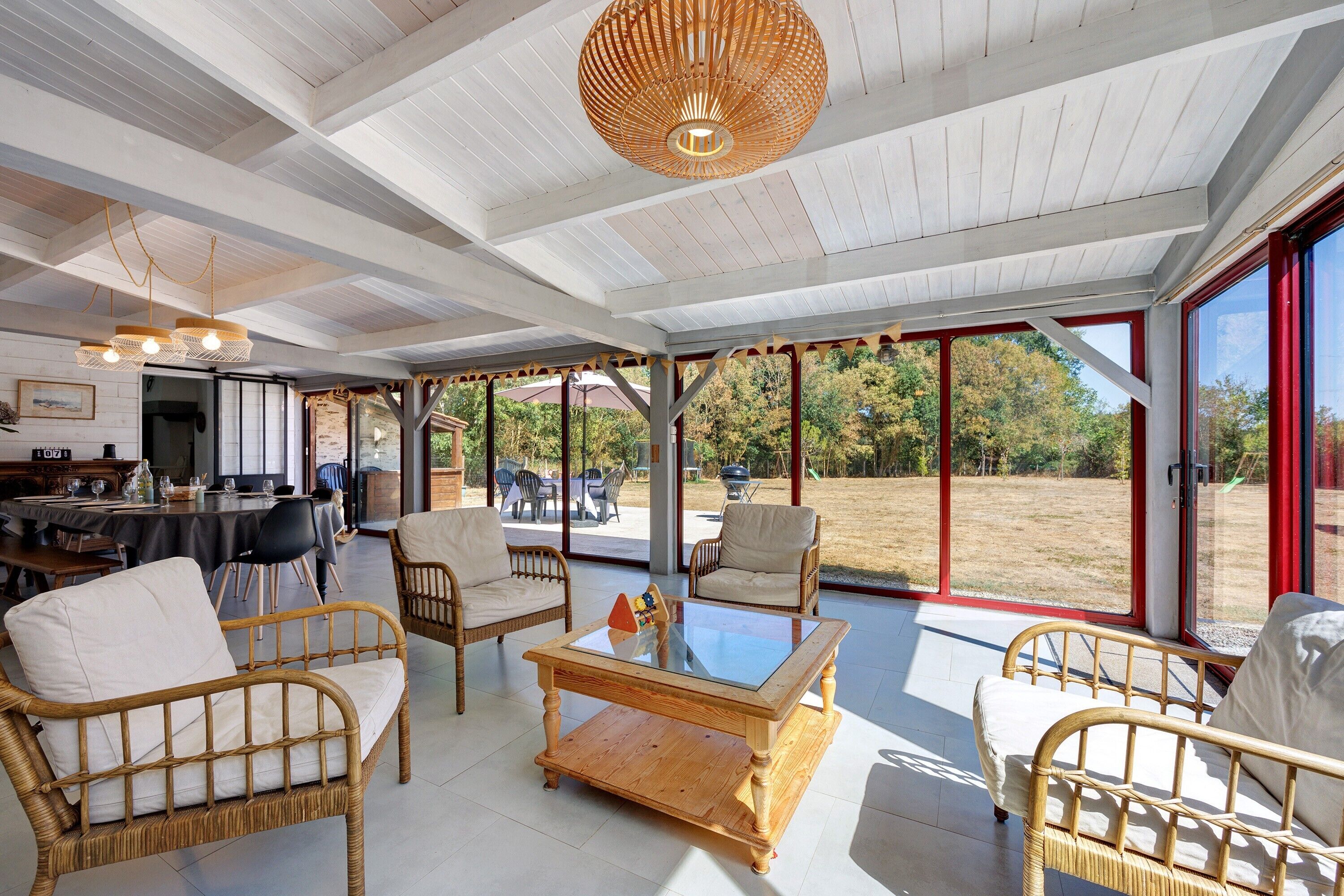 A spacious indoor area with wicker furniture, a glass coffee table, and a ceiling with exposed beams.