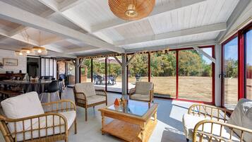 A spacious indoor area with wicker furniture, a glass coffee table, and a ceiling with exposed beams.