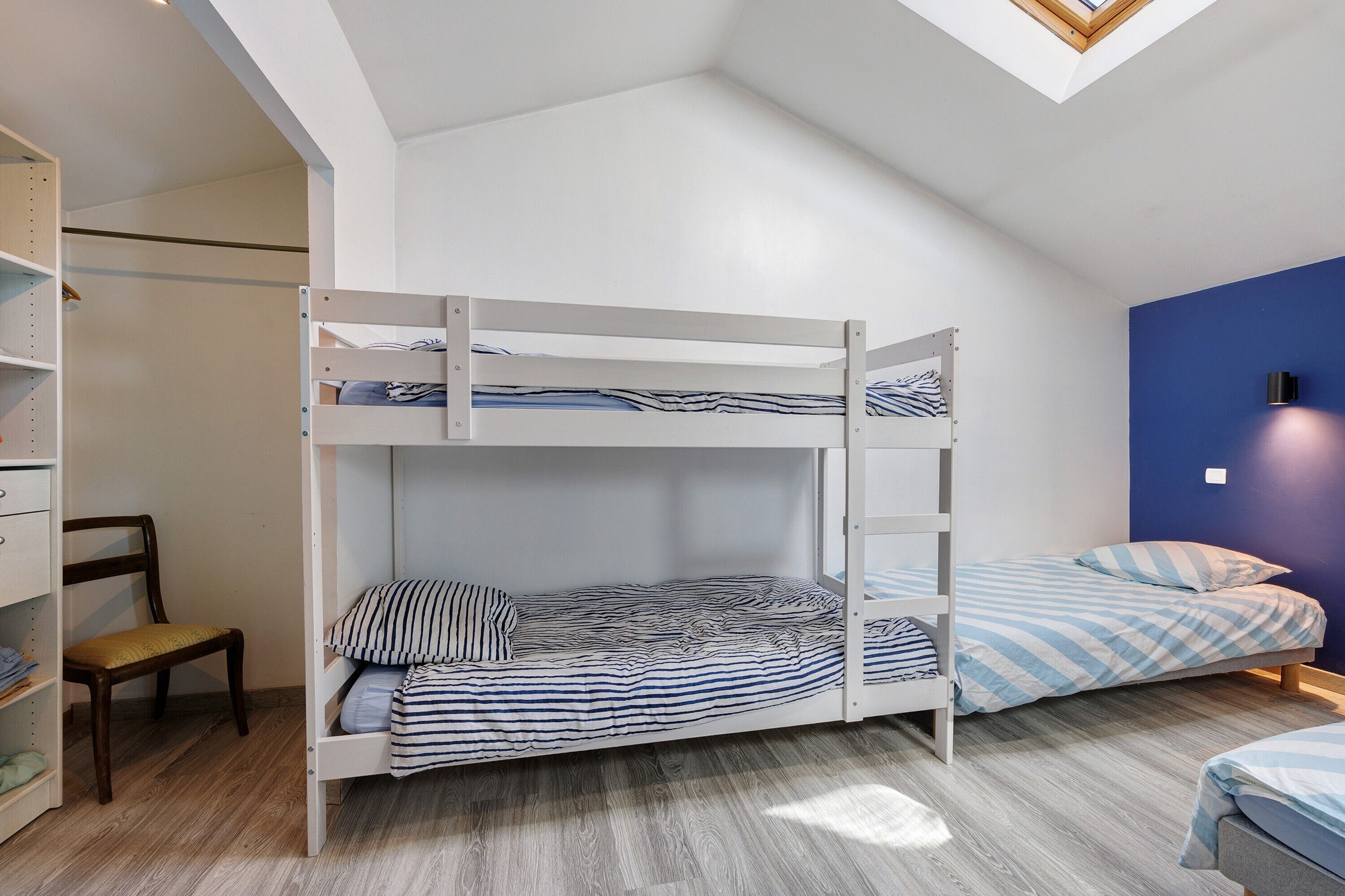 Une chambre avec un lit superposé, une lucarne, un plancher en bois et un mur d’accent bleu.