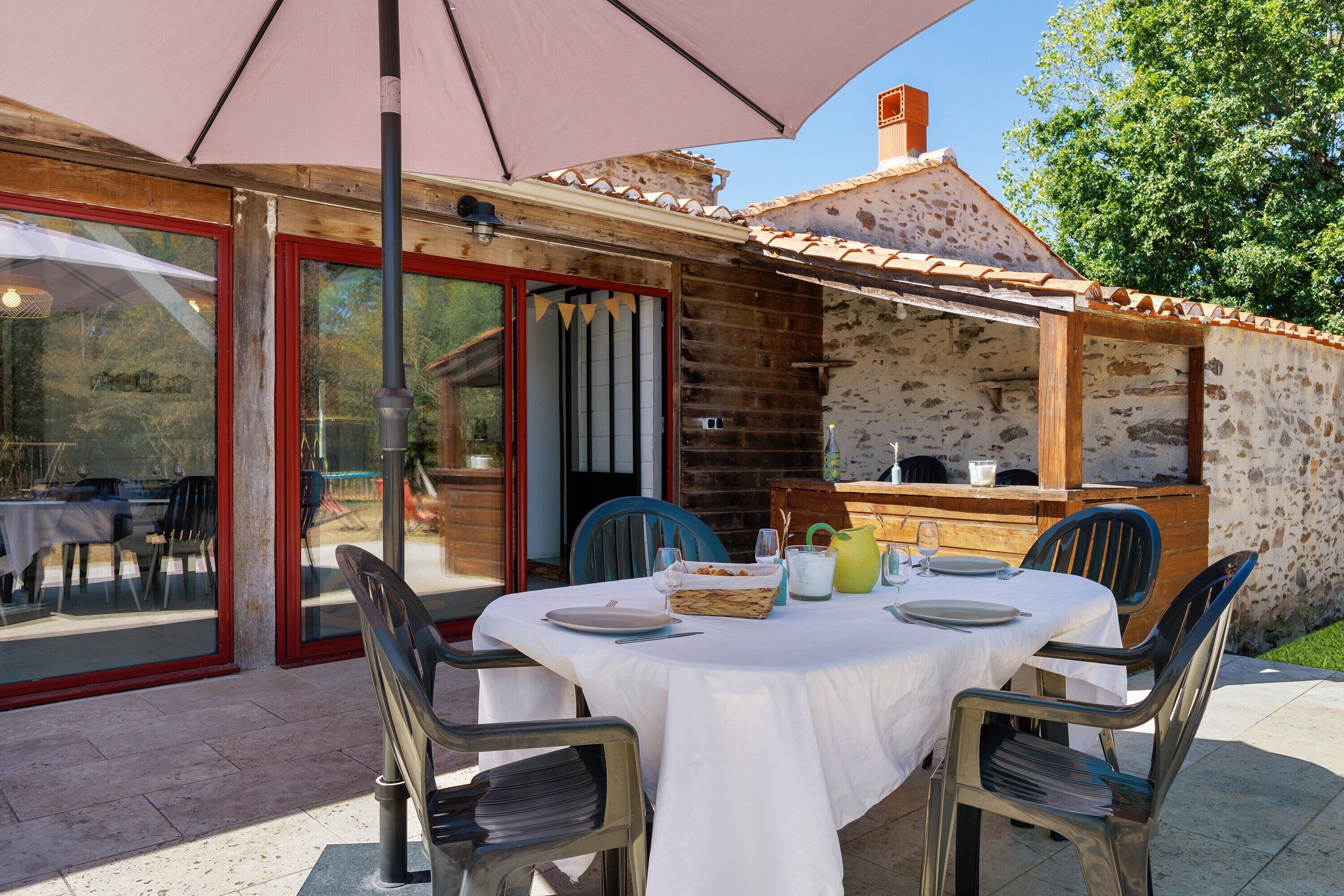 Un espace de restauration en plein air avec une table dressée pour deux personnes, entourée de chaises, et un grand parasol offrant de l’ombre.