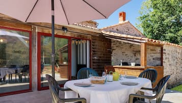 Un'area pranzo all'aperto con un tavolo apparecchiato per due persone, circondato da sedie e ombreggiato da un grande ombrellone.