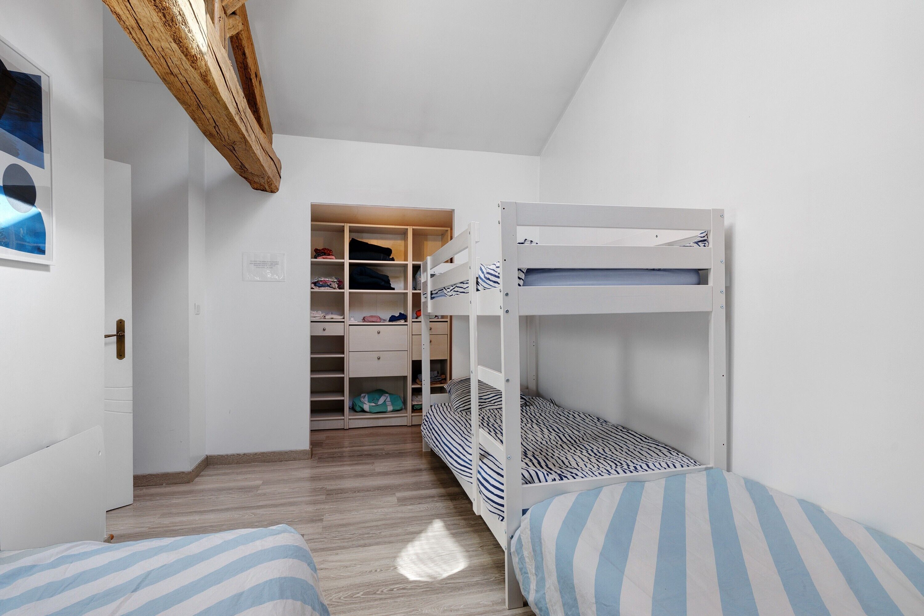 A bedroom with a bunk bed, a wooden wardrobe, and a small closet with shelves.