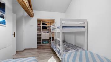 A bedroom with a bunk bed, a wooden wardrobe, and a small closet with shelves.