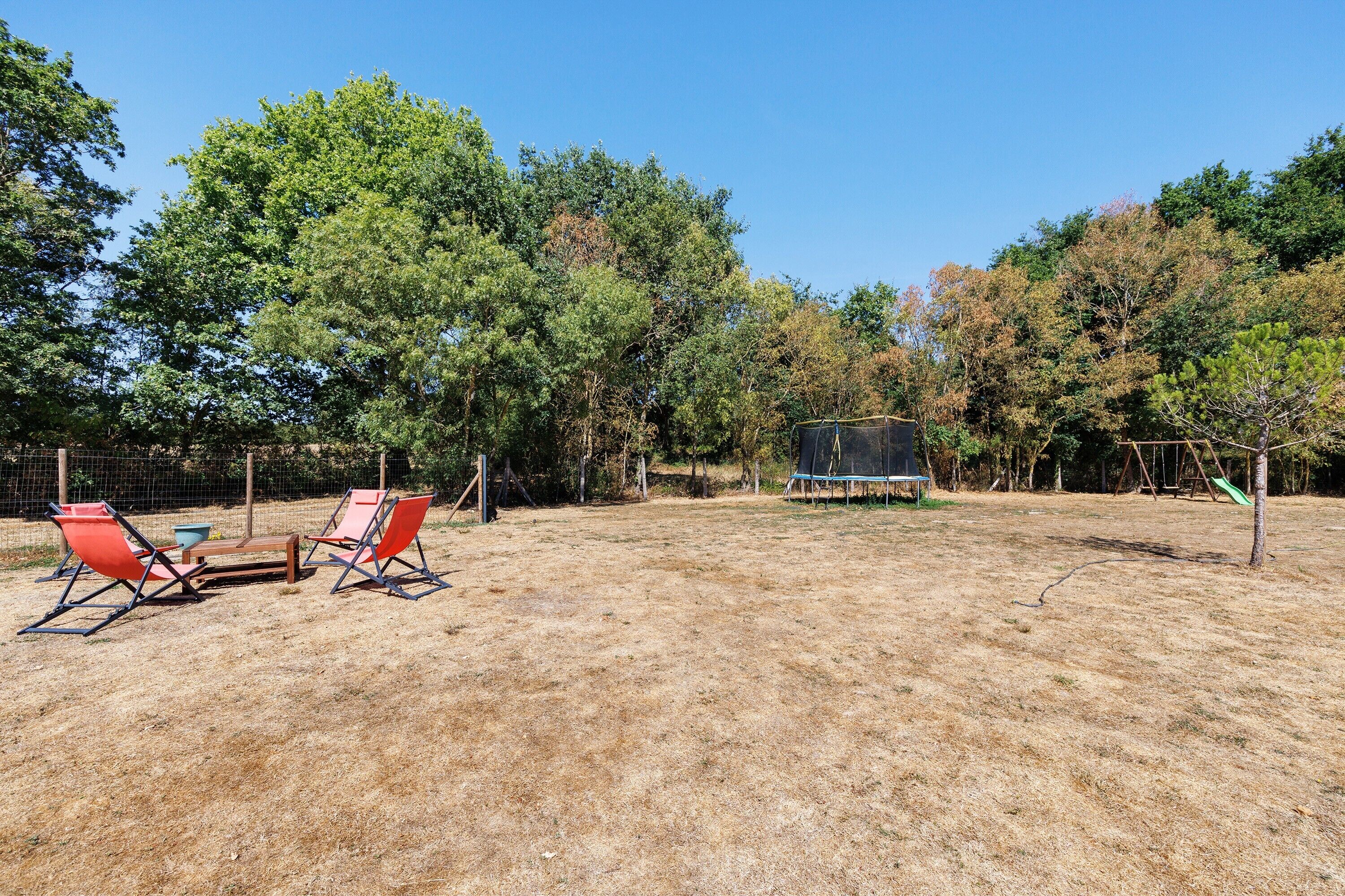 An outdoor area with a trampoline, two red chairs, and a table.