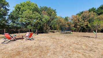 An outdoor area with a trampoline, two red chairs, and a table.