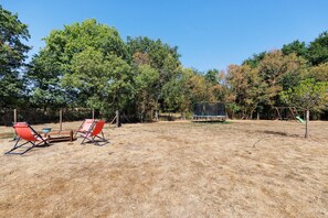 An outdoor area with a trampoline, two red chairs, and a table.