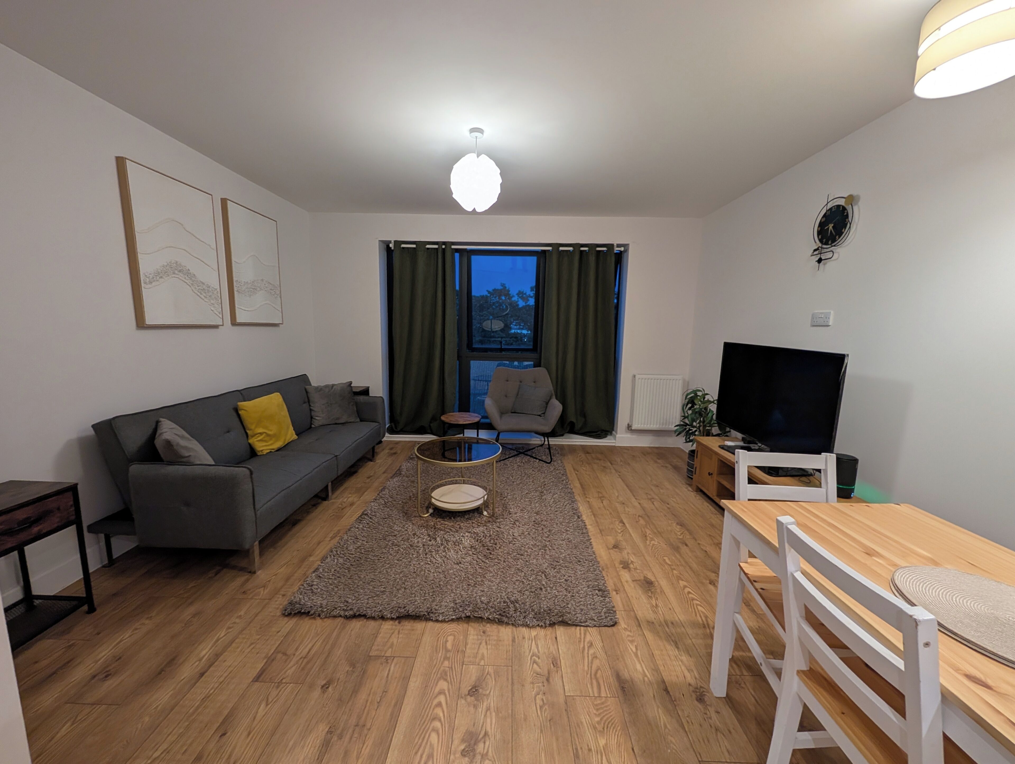 Una sala de estar moderna con sofá, sillón, mesa de centro, televisor y mesa de comedor.