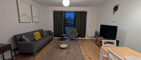 Una sala de estar moderna con sofá, sillón, mesa de centro, televisor y mesa de comedor.