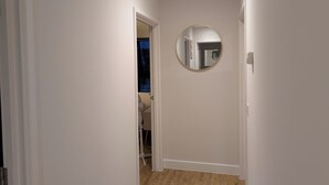 Kapea käytävä, jonka seinät ovat valkoiset, lattia puuta ja seinällä pyöreä peili.