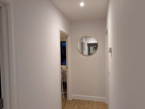 A narrow hallway with white walls, a wooden floor, and a round mirror on the wall. - 2 Bedroom Apartment at North Farm road, Royal Tunbridge Wells United Kingdom (Royal Tunbridge Wells)