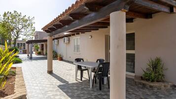 Ein möblierter Patio-Bereich mit Tisch und Stühlen, umgeben von Blumentöpfen und einem gefliesten Boden.