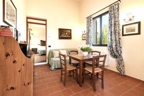 A dining area with a table and chairs, a window with patterned curtains, and a painting on the wall. - Gaetano Spadaro Estate, Moraiolo Apartment (Capannori)