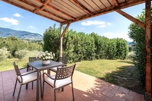 Eine Terrasse im Freien mit Tisch und Stühlen, umgeben von Grünpflanzen und Blick auf ferne Hügel.