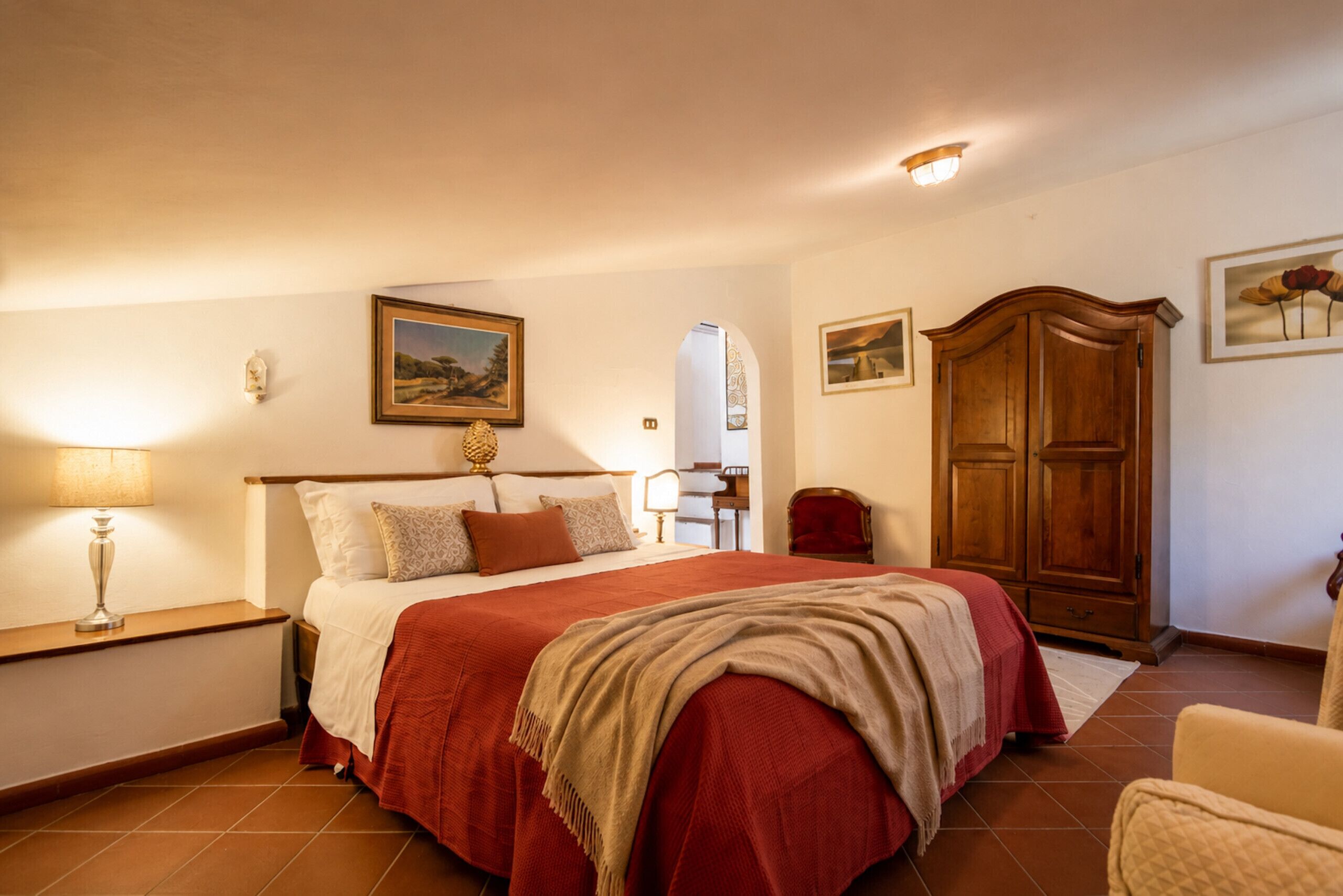 A bedroom with a large bed, a wooden wardrobe, a nightstand, and a lamp.