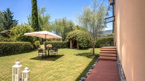 A well-maintained garden with a patio table and chairs, a white umbrella, and two lanterns. - Gaetano Spadaro Estate, Pendolino Apartment (Capannori)