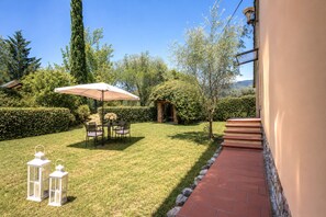 Ein gepflegter Garten mit Terrassentisch, Stühlen, einem weißen Sonnenschirm und zwei Laternen.