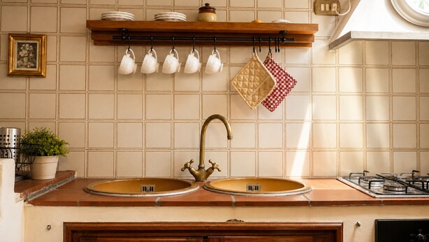 A kitchen with a double sink, a gas stove, a hanging pot rack, and a potted plant. - Gaetano Spadaro Estate, Pendolino Apartment (Capannori)